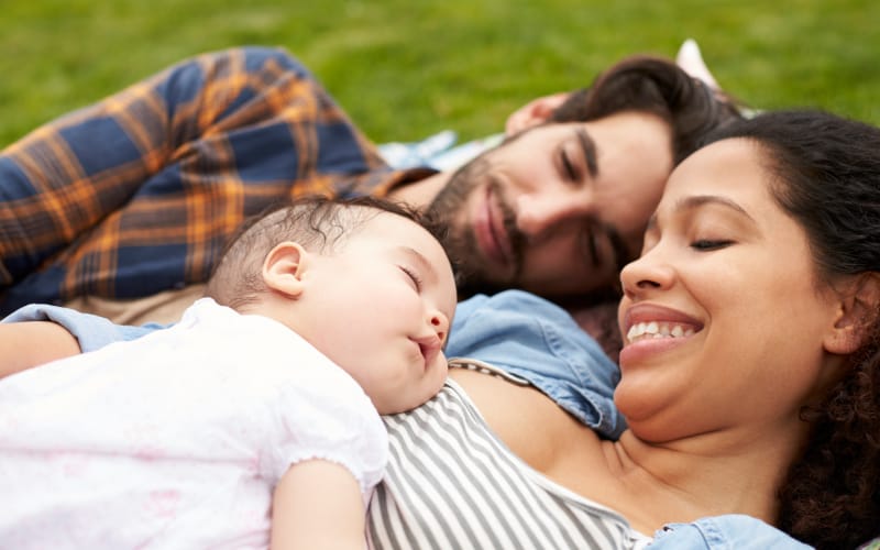A mixed-race couple cuddles their infant at the park